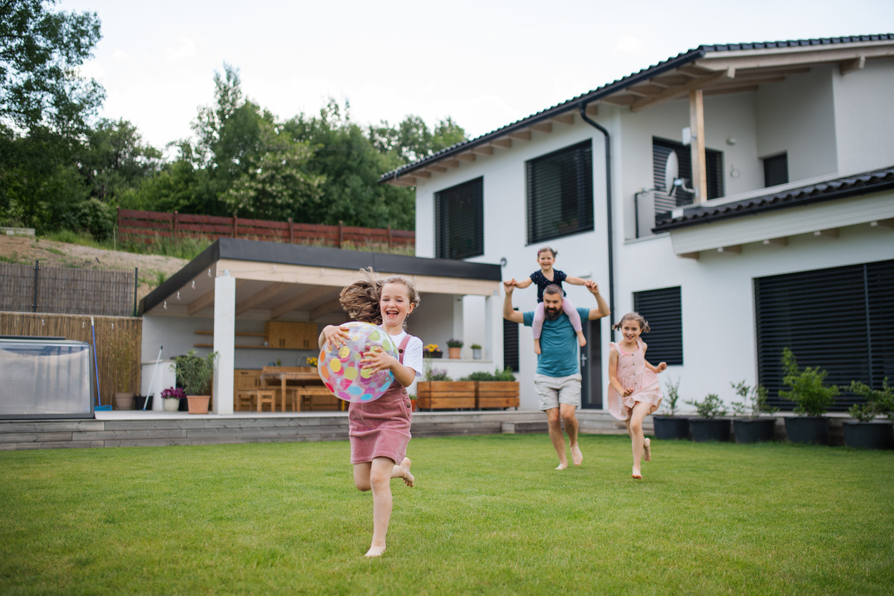 Famille courant sur une pelouse devant une maison moderne, illustrant la protection et la sécurité offertes par l’assurance des particuliers.