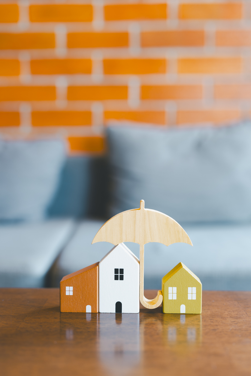 Home represented by miniature houses sheltered under an umbrella, evoking safety and protection in home insurance. Home represented by miniature houses sheltered under an umbrella, evoking safety and protection in home insurance.