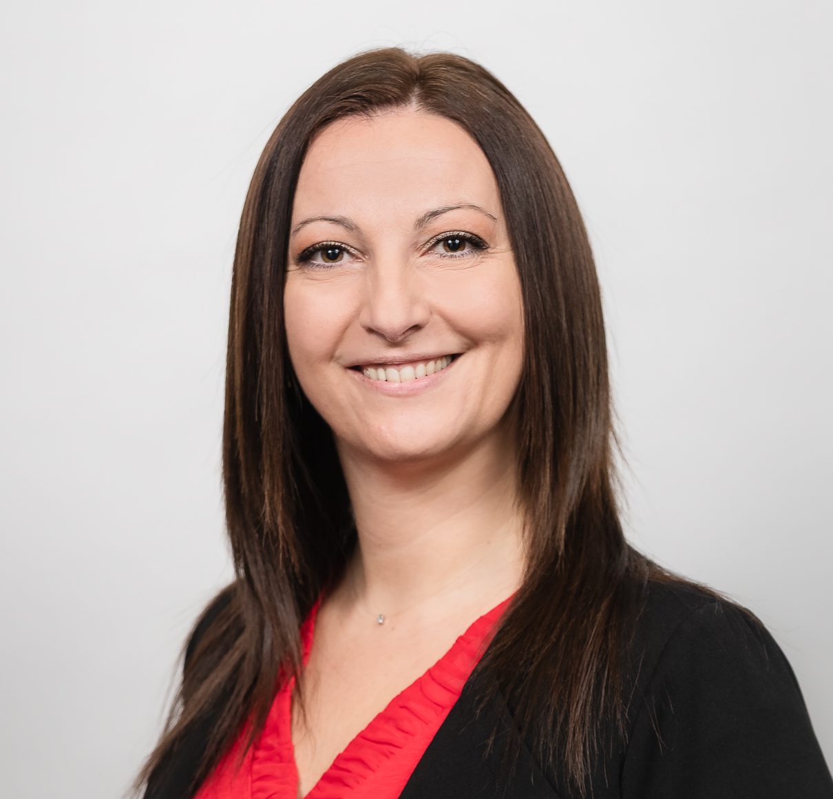 Professional headshot of Magalie Rouillot, CPHR, Director of Talent Acquisition at La Turquoise. Magalie Rouillot is photographed against a light gray background, with shoulder-length dark brown hair, wearing a red top and a black blazer. The studio portrait is framed from the mid-torso up with even lighting.
