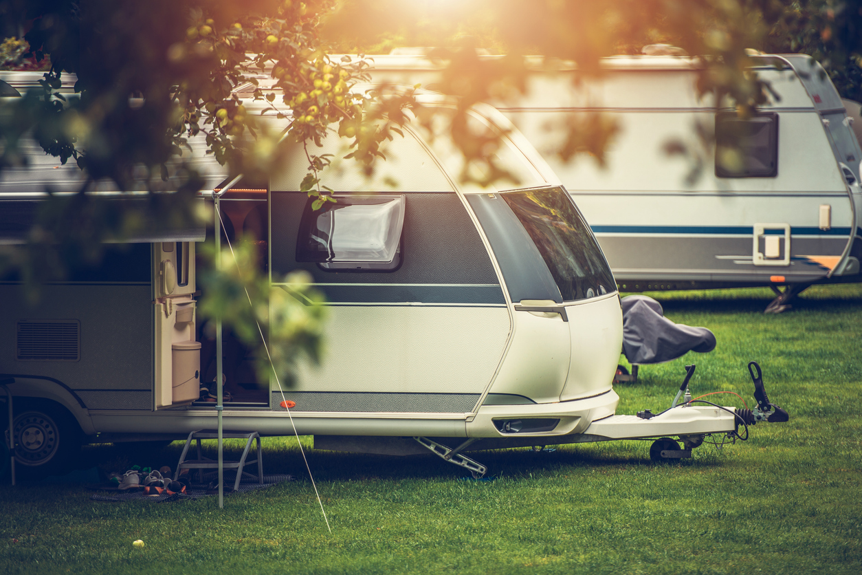 Camping trailer and camping trailer hitch aligned on a lush green site, illuminated by natural light. Typical usage context for trailer insurance.