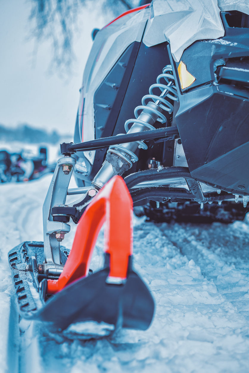 Vue rapprochée du ski et de la suspension d’une motoneige sur la neige. Véhicule de loisir nécessitant une assurance adaptée.