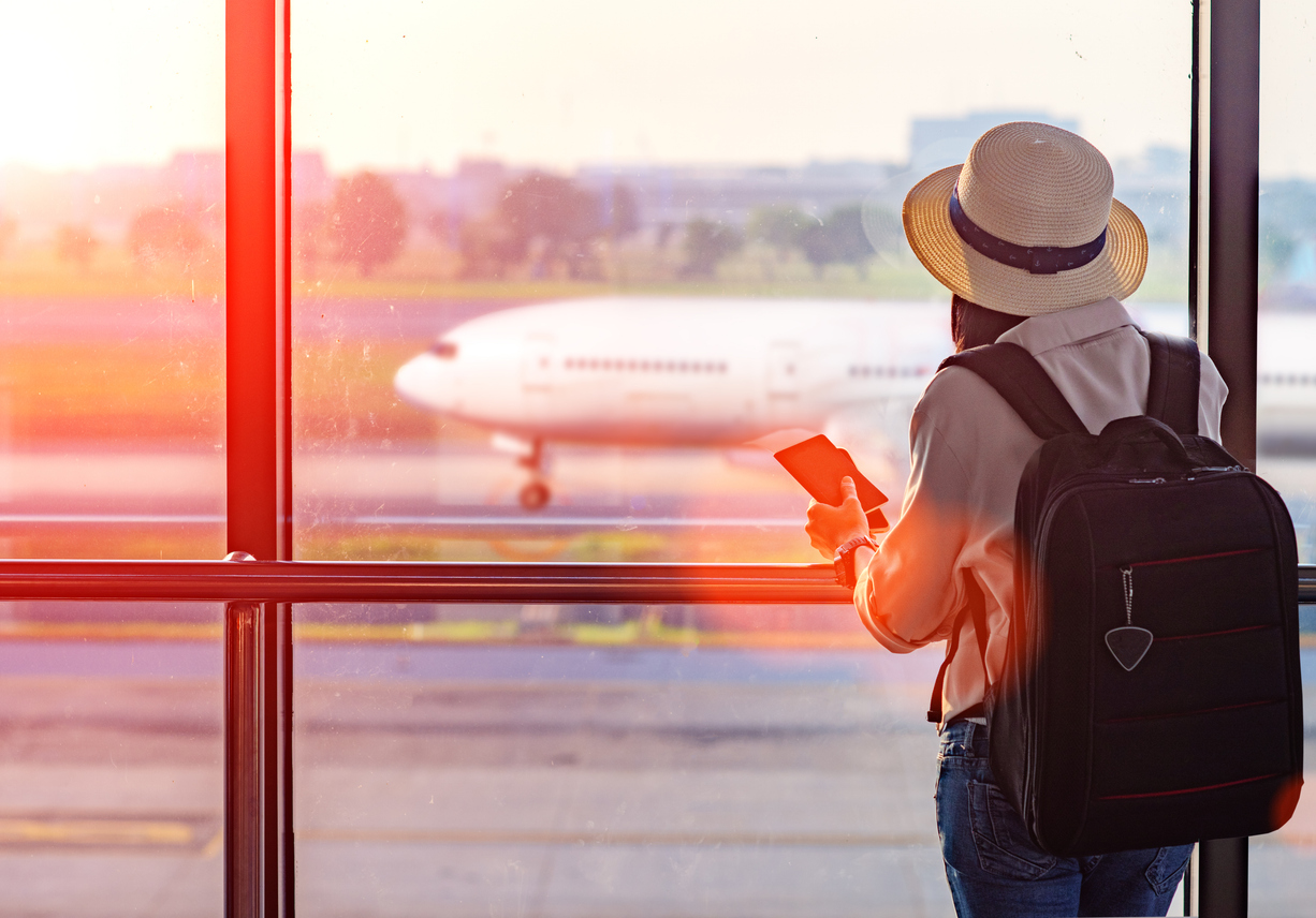 Traveler with a backpack holding travel documents in an airport terminal, airplane visible on the tarmac. Travel insurance before a departure abroad.