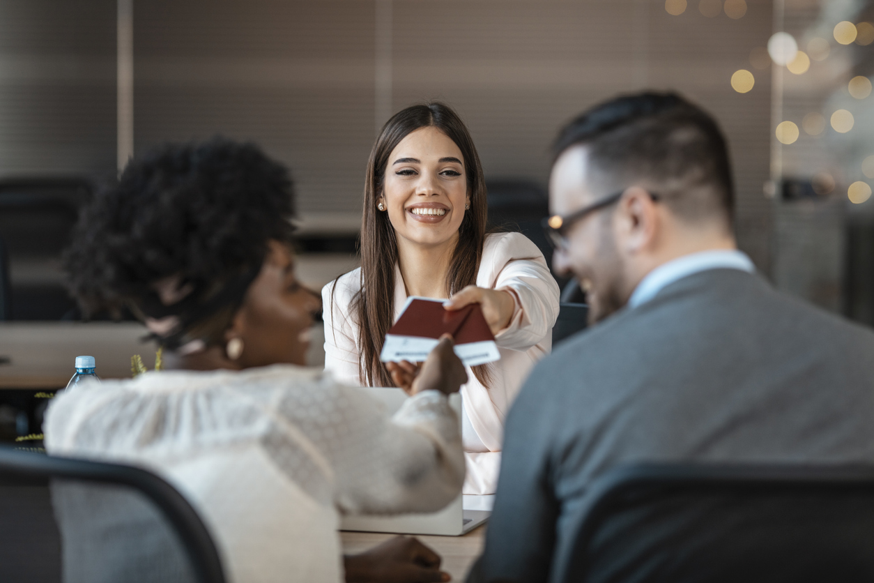 Conseiller en agence de voyages remettant des documents de voyage à des clients lors d’une consultation au bureau. Contexte de planification de séjour et d’assurance voyage au Québec.