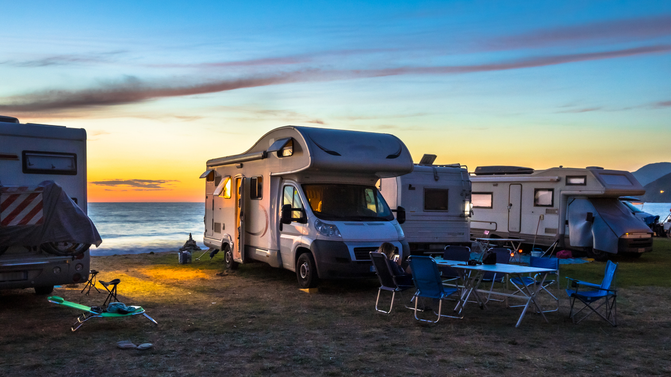 Caravane et autocaravane regroupées dans un camping avec tables et chaises extérieures. Contexte de voyage et de plein air associé à l’assurance caravane.
