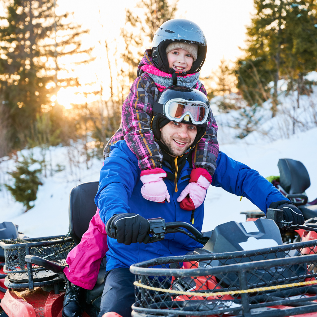 All-terrain vehicle driven on a snow-covered forest trail with a rear passenger. Illustration of family use requiring appropriate ATV insurance.
