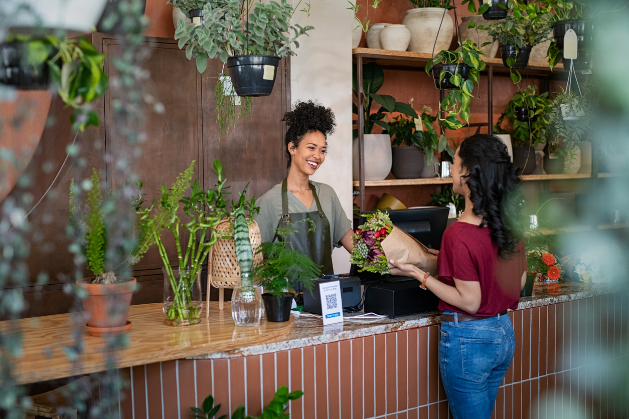 Transaction entre un client et un commerçant dans une boutique de fleurs avec plantes exposées sur des étagères. Illustration d’un commerce de détail et de la protection d’assurance pour entreprises au Québec.