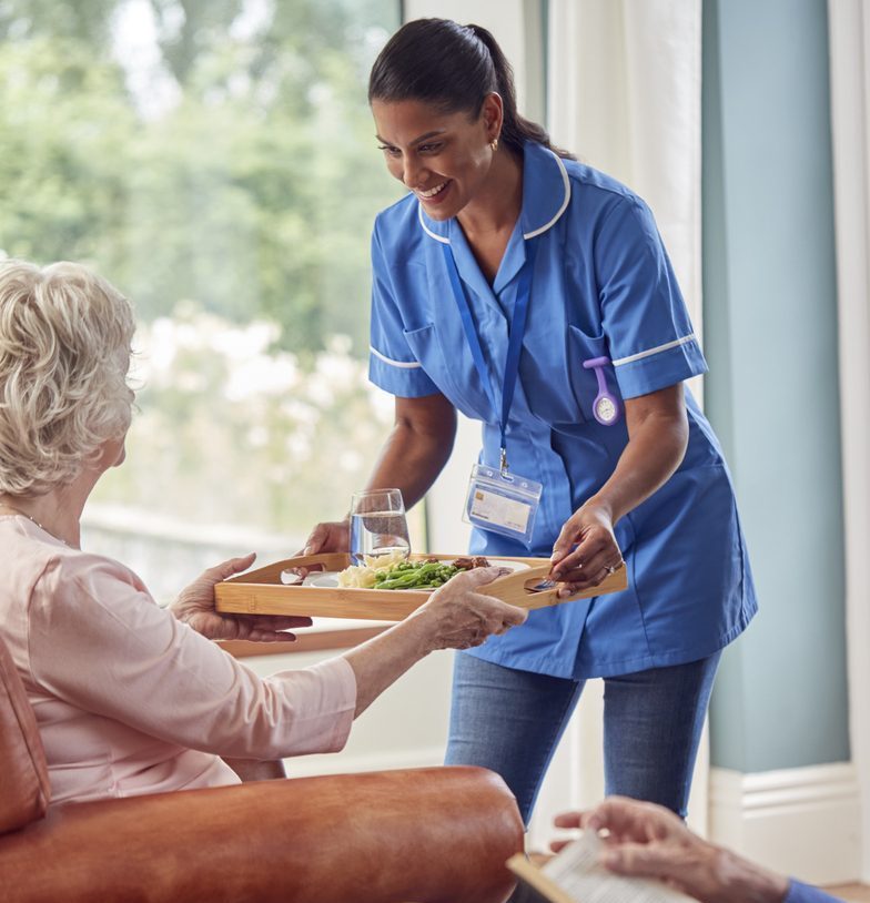 Personnel soignant servant un repas dans un environnement chaleureux de résidence pour personnes âgées. Couverture d'assurance pour les résidences privées pour aînés.
