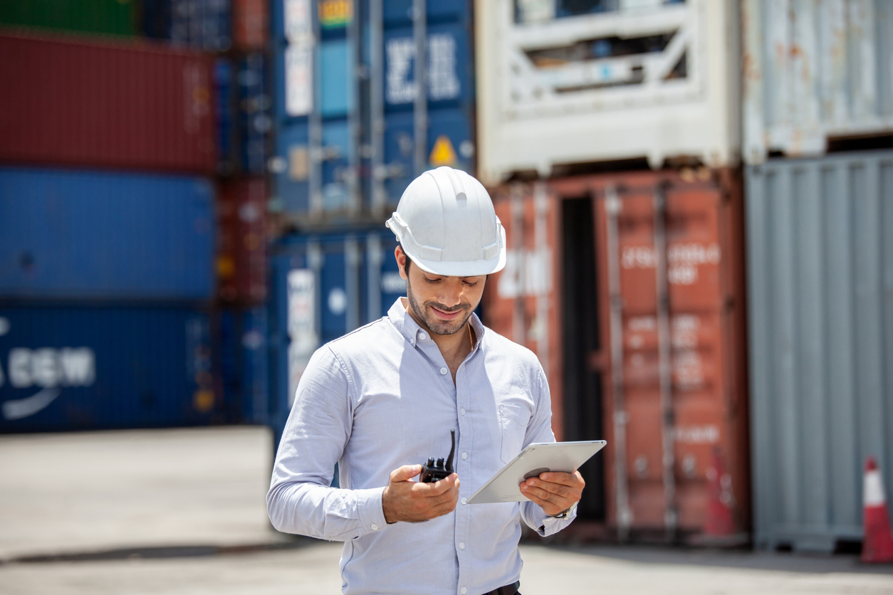 Entrepreneur manufacturier portant un casque de sécurité et utilisant des outils numériques à l’extérieur d’une usine. Situation liée à l’assurance responsabilité civile des entreprises manufacturières au Québec.