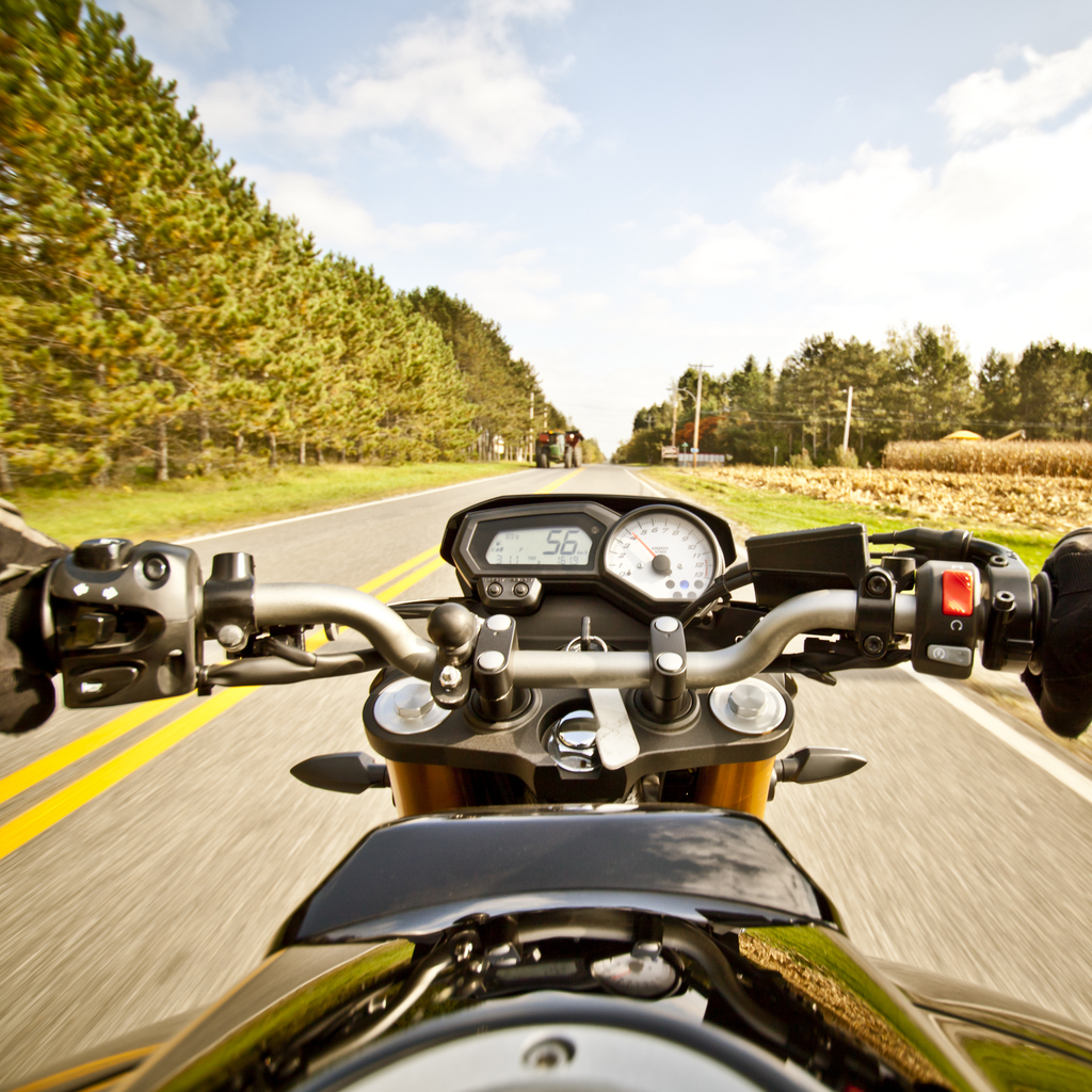Riding a motorcycle on an open road in a rural setting. Representation of a seasonal vehicle covered by motorcycle and three‑wheeler insurance.