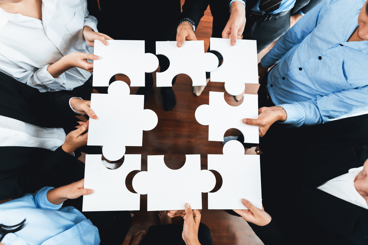 Mains de plusieurs partenaires d’assurance assemblant des pièces de puzzle. Représentation de la coordination et de l’expertise partagée en assurances au Québec.