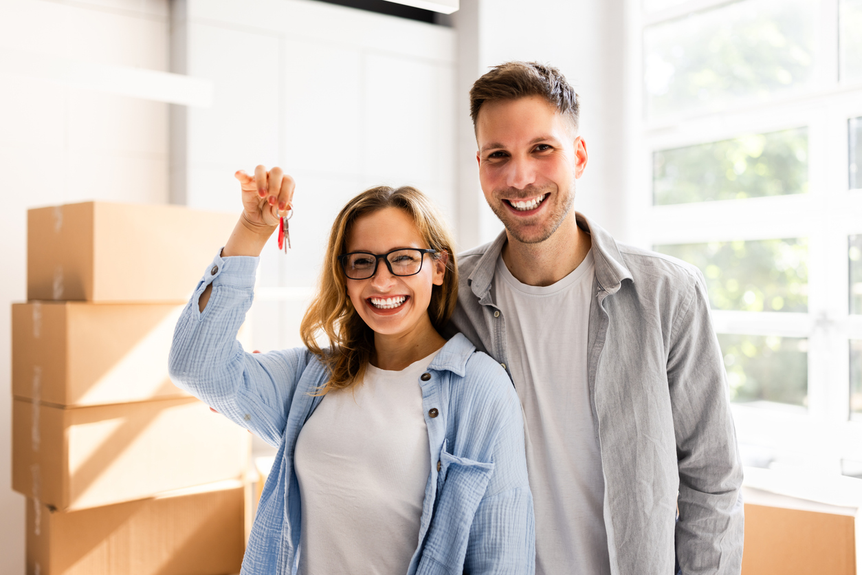 New homeowners holding keys inside a house with moving boxes. A typical situation covered by homeowners insurance.