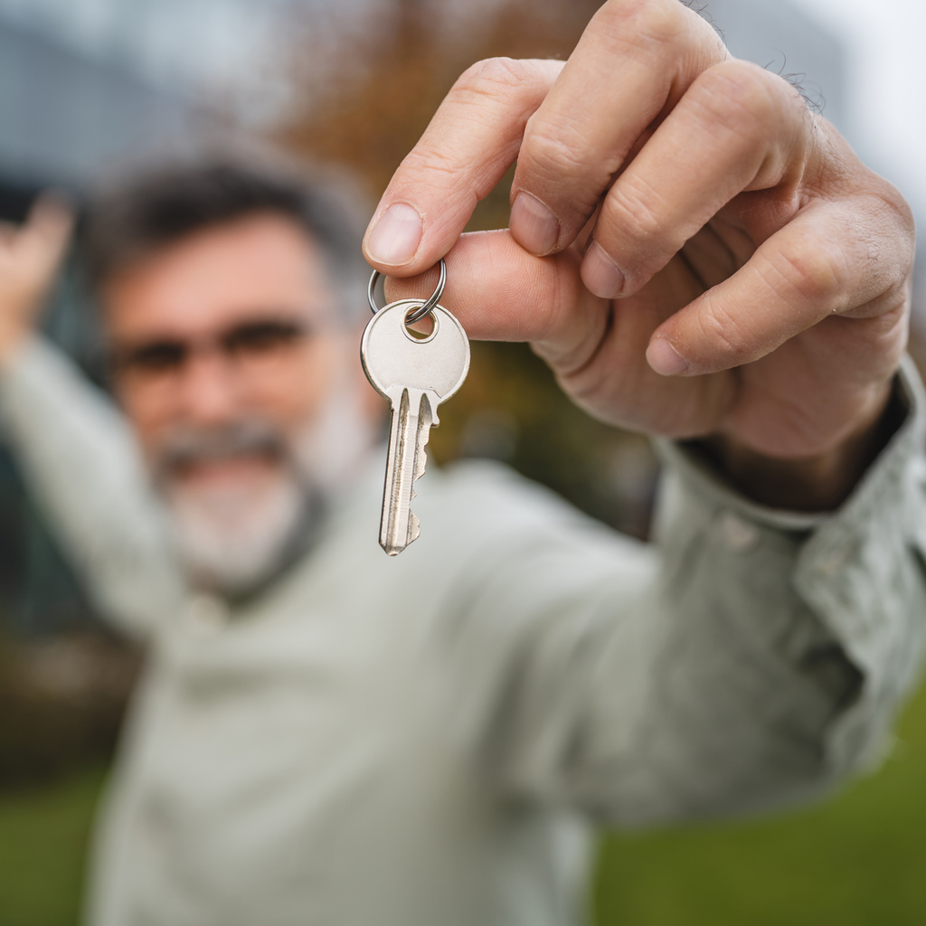 Keys being handed over for a rental property, with a residential building blurred in the background. Context related to tenant insurance.