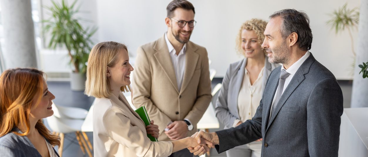 Investisseur serrant la main d’une partenaire devant une équipe en bureau, illustrant les ententes d’affaires et l’assurance responsabilité professionnelle au Québec.
