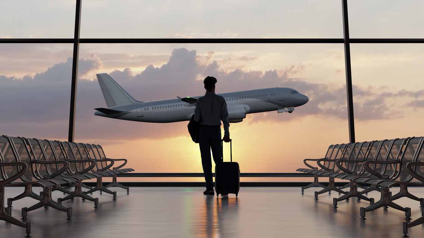 Traveler with a suitcase in an airport, airplane visible outside the terminal. Illustration related to travel insurance before a departure abroad.