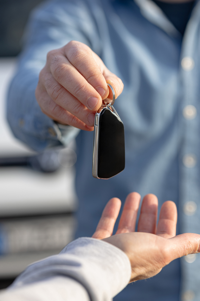 Transmission d’une clé de voiture entre deux personnes, près d’un véhicule. Visuel associé à l’assurance de remplacement après une perte ou un sinistre.