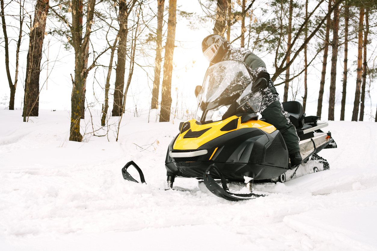 Snowmobile used on a snow-covered terrain surrounded by trees. Typical context of winter travel covered by snowmobile insurance.