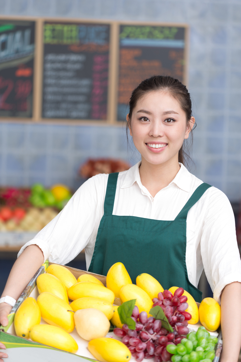 Détaillant en fruits et légumes tenant une caisse de produits frais derrière le comptoir d’une boutique. Contexte d’activités commerciales nécessitant une assurance pour commerçants au Québec.