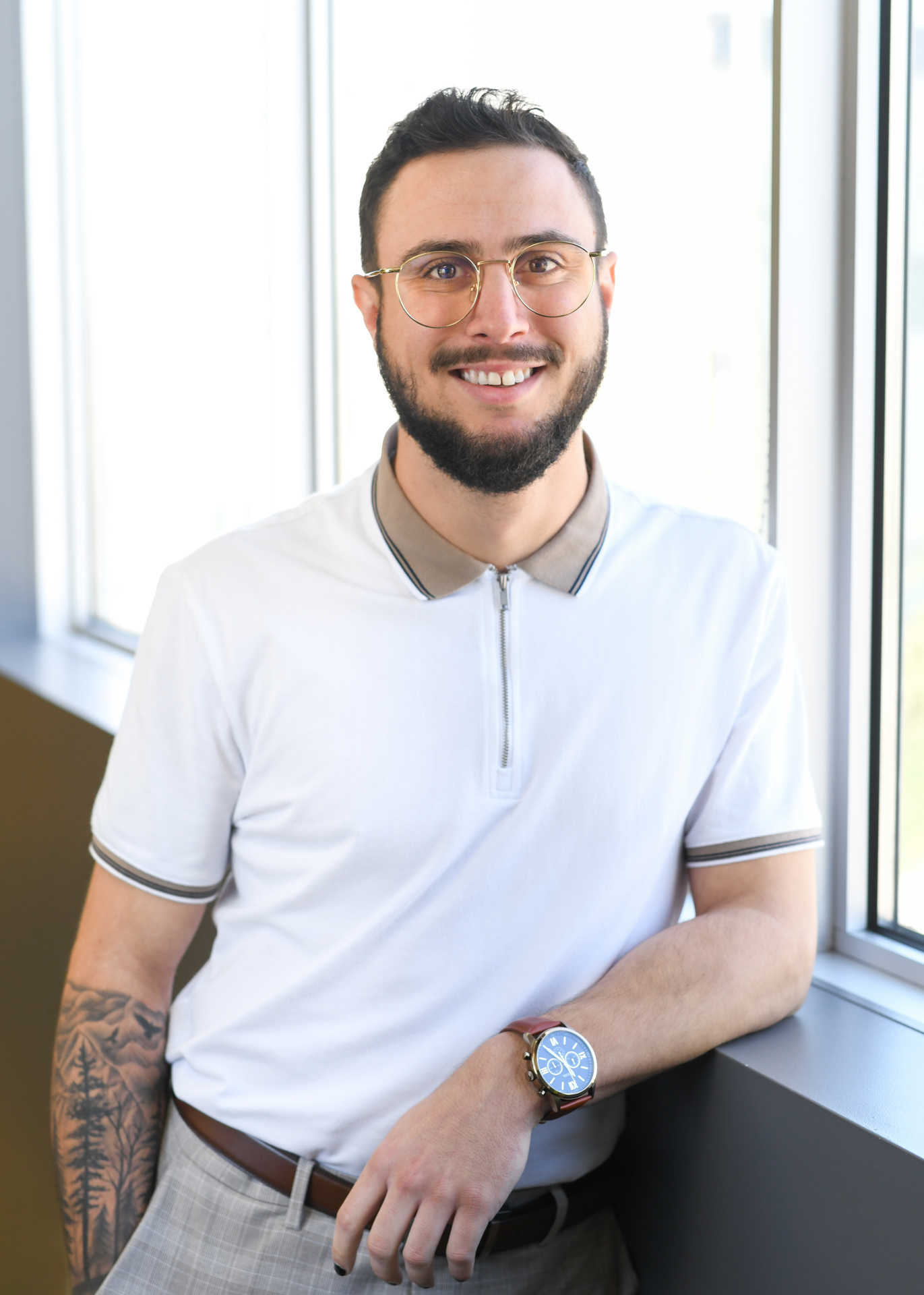 Portrait de Félix Ducharme, conseiller en ressources humaines au Cabinet La Turquoise, debout près d’une fenêtre dans un bureau lumineux, portant des lunettes, un polo clair et une montre.